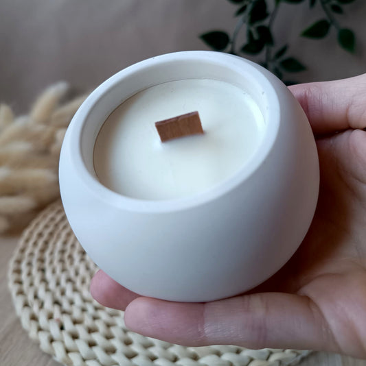 Vela decorativa redonda pequeña de soja en recipiente blanco liso de resina mineral sostenida en la mano con fondo neutro