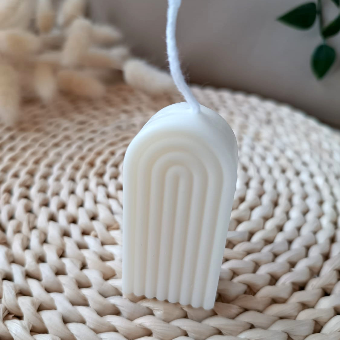 Vela decorativa natural de soja en forma de arco con líneas verticales estilo minimalista, sobre base de fibras naturales y fondo neutro