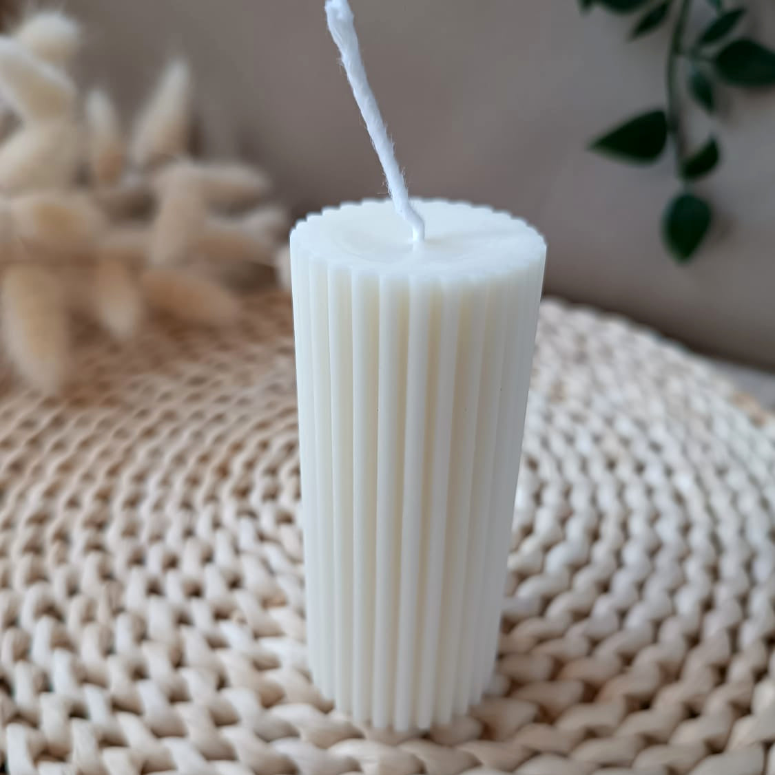 Vela decorativa natural de soja tipo pilar cilíndrica con textura acanalada vertical estilo minimalista, sobre fibras naturales y fondo neturo