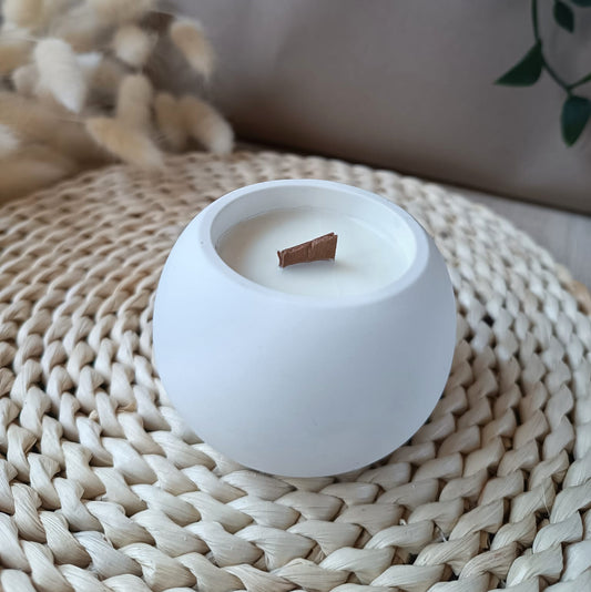 Vela pequeñas redondas de soja en recipiente blanco liso de resina mineral con mecha de madera sobre base de fibras naturales y fondo neutro