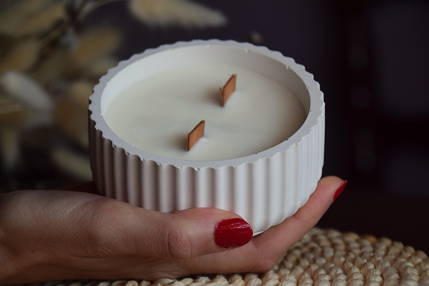 Vela decorativa en cuenco acanalado con mechas de madera sujetado por mano de modelo y fondo rustico.