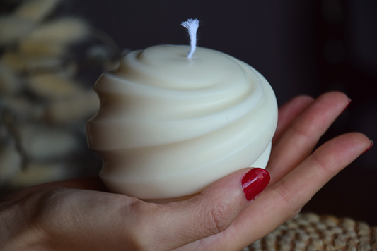 Vela decorativa grande en forma de tirabuzon y pabilo de algodon, sujetada por mano de modelo con fondo rustico.