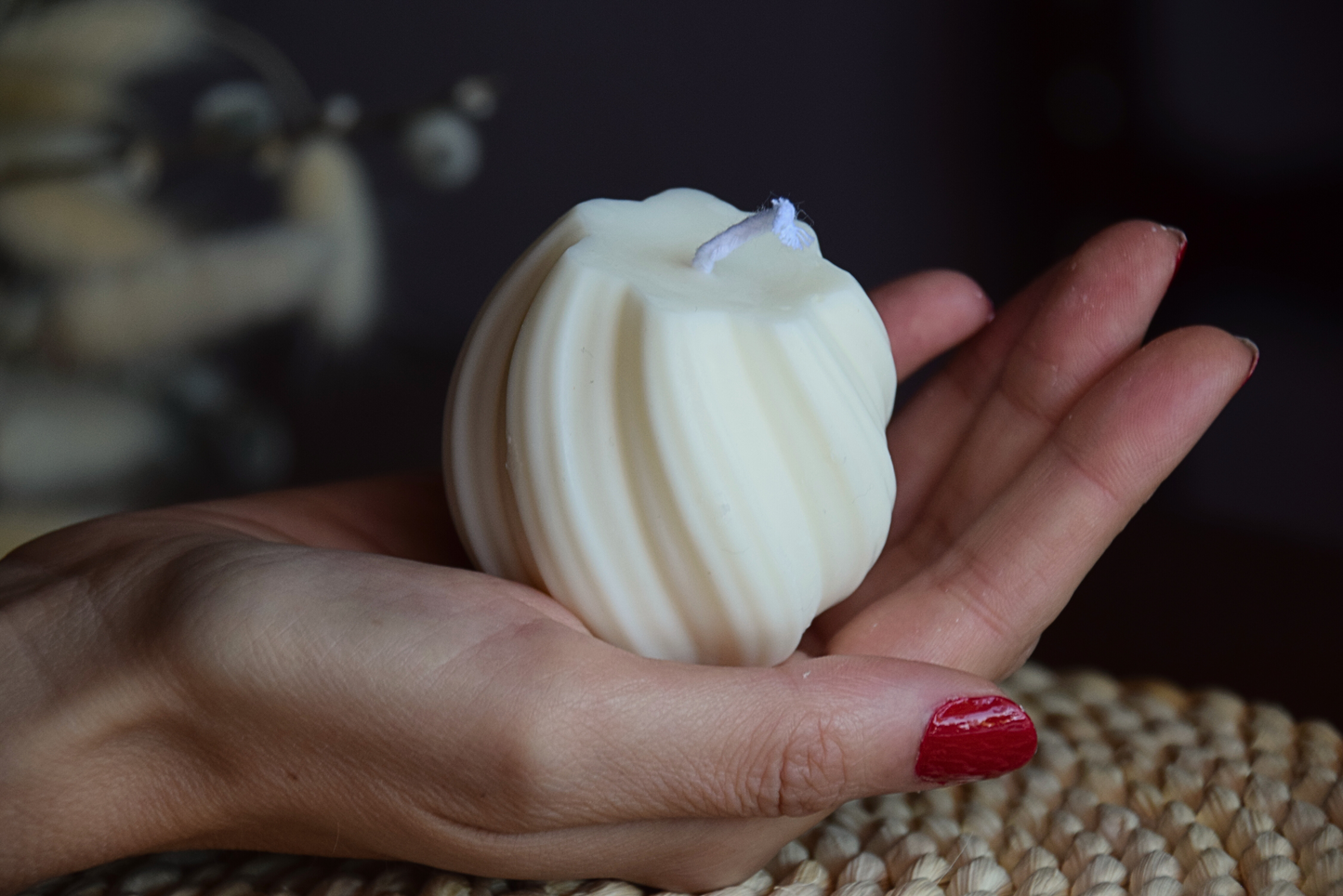 Vela decorativa pequeña en forma de tirabuzon con pabilo de algodon, sujetada por mano de modelo y presentada en fondo rustico.