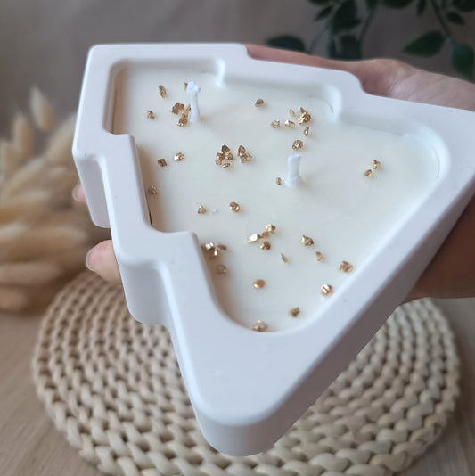 Vela de soja en forma de árbol en recipiente de resina mineral blanco con detalles dorados sostenida en la mano y fondo neutro