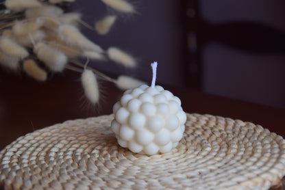 Vela decorativa perqueña con forma redonda, con burbujas y pabilo de algodon en fondo rustico. 