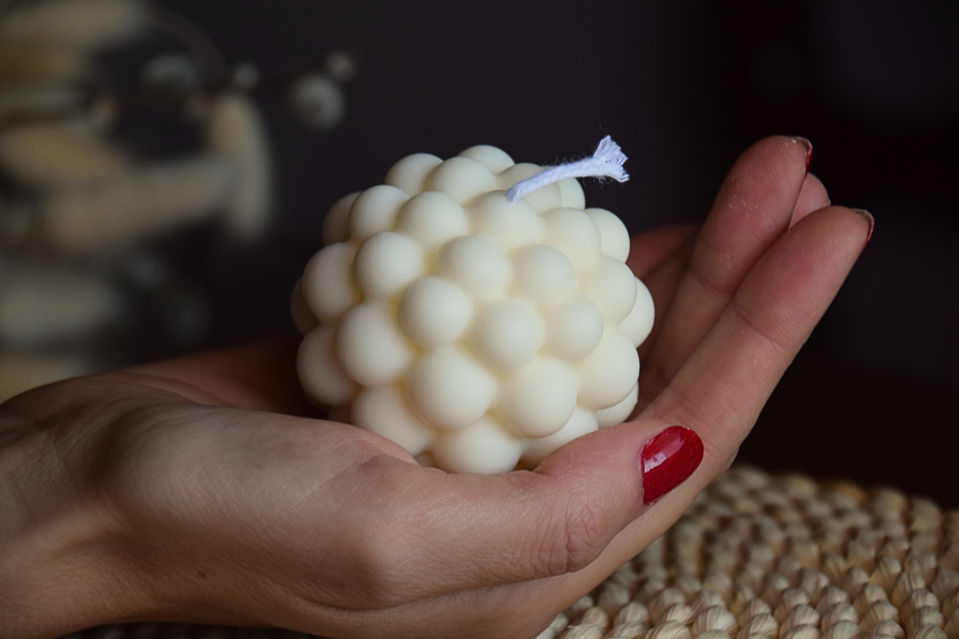 Vela decorativa perqueña con forma redonda, con burbujas y pabilo de algodon sujetada por mano de modelo en fondo rustico. 