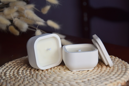 Vela decorativa en caja perqueña de color blanco con fondo rustico.