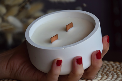 Vela decorativa en cuenco liso con mechas de madera sujetado por mano de modelo con fondo rustico.