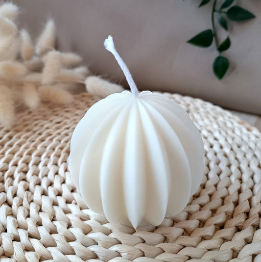 Vela decorativa natural de soja en forma de esfera geométrica estilo minimalista, sobre base de fibras naturales y fondo neutro