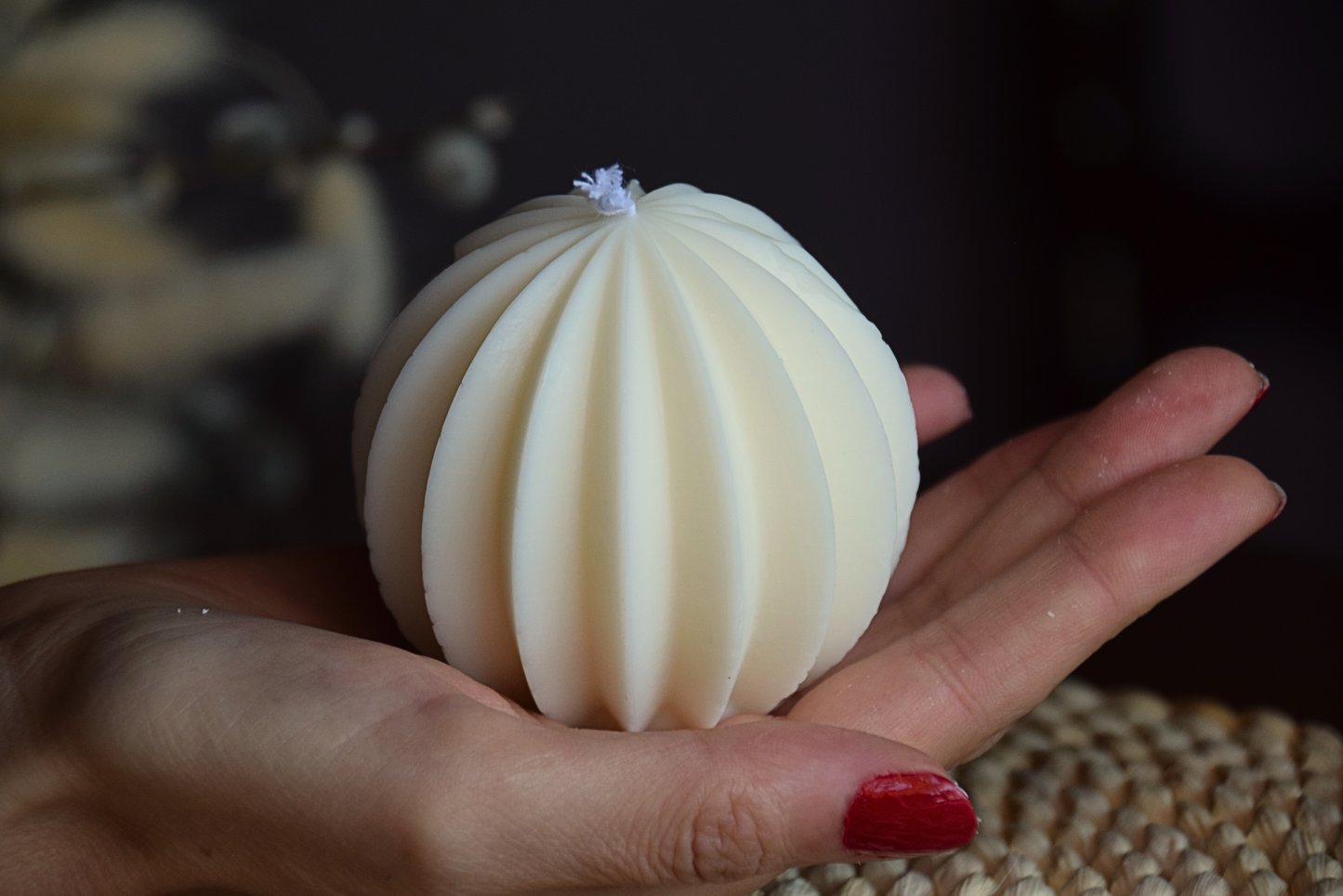 Vela decorativa redonda con forma geometrica y pabilo de algodon sujeta por mano de modelo en fondo rustico.