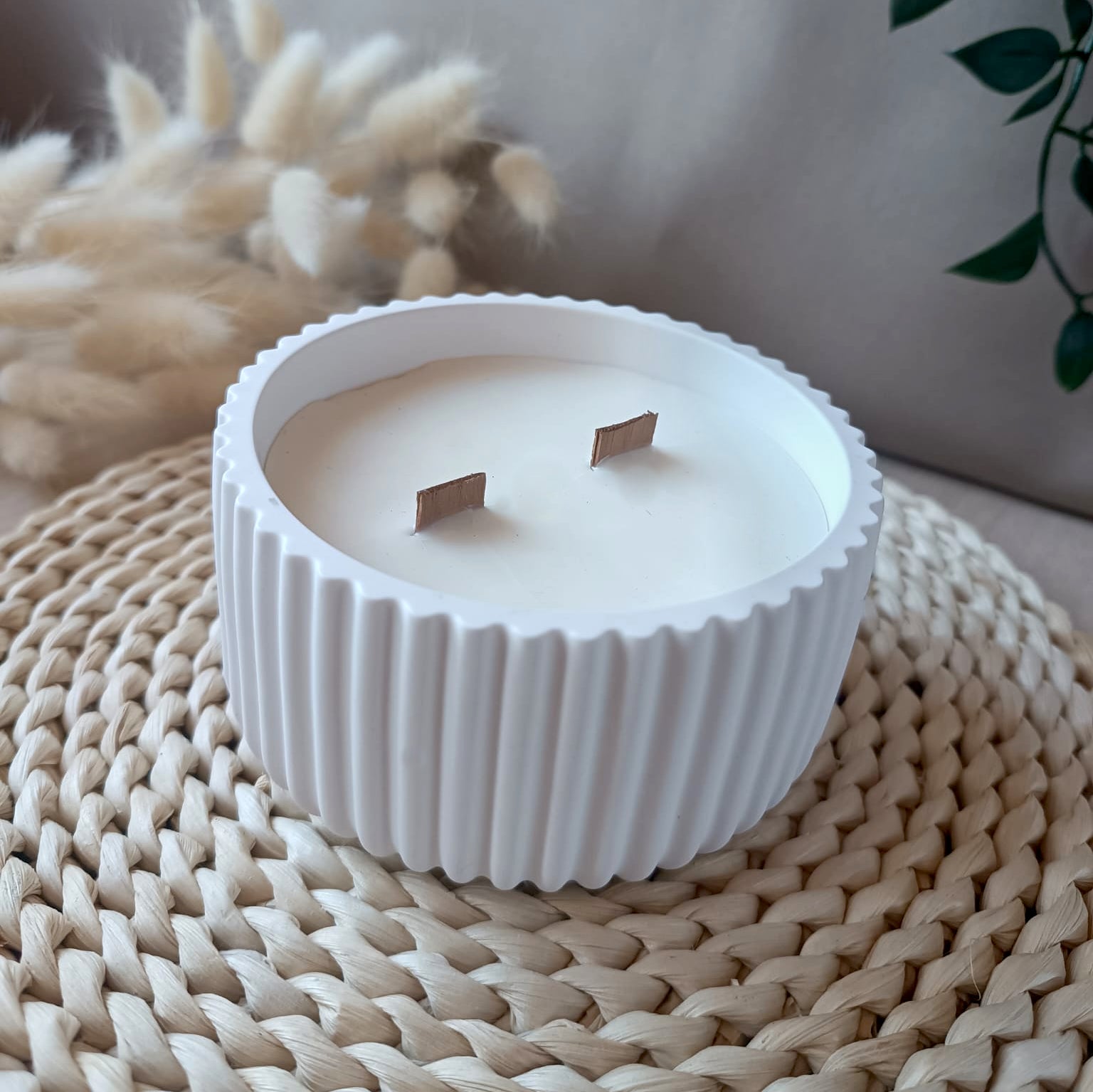 Vela artesanal grande de soja en recipiente blanco con textura de rayas y doble mecha de madera sobre base de fibras naturales y fondo neutro