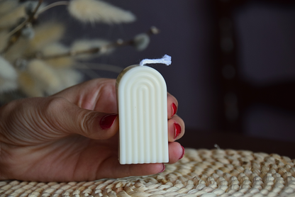 Vela decorativa mini arco con pabilo de algodon, sujetada por mano de modelo en fondo rustico.