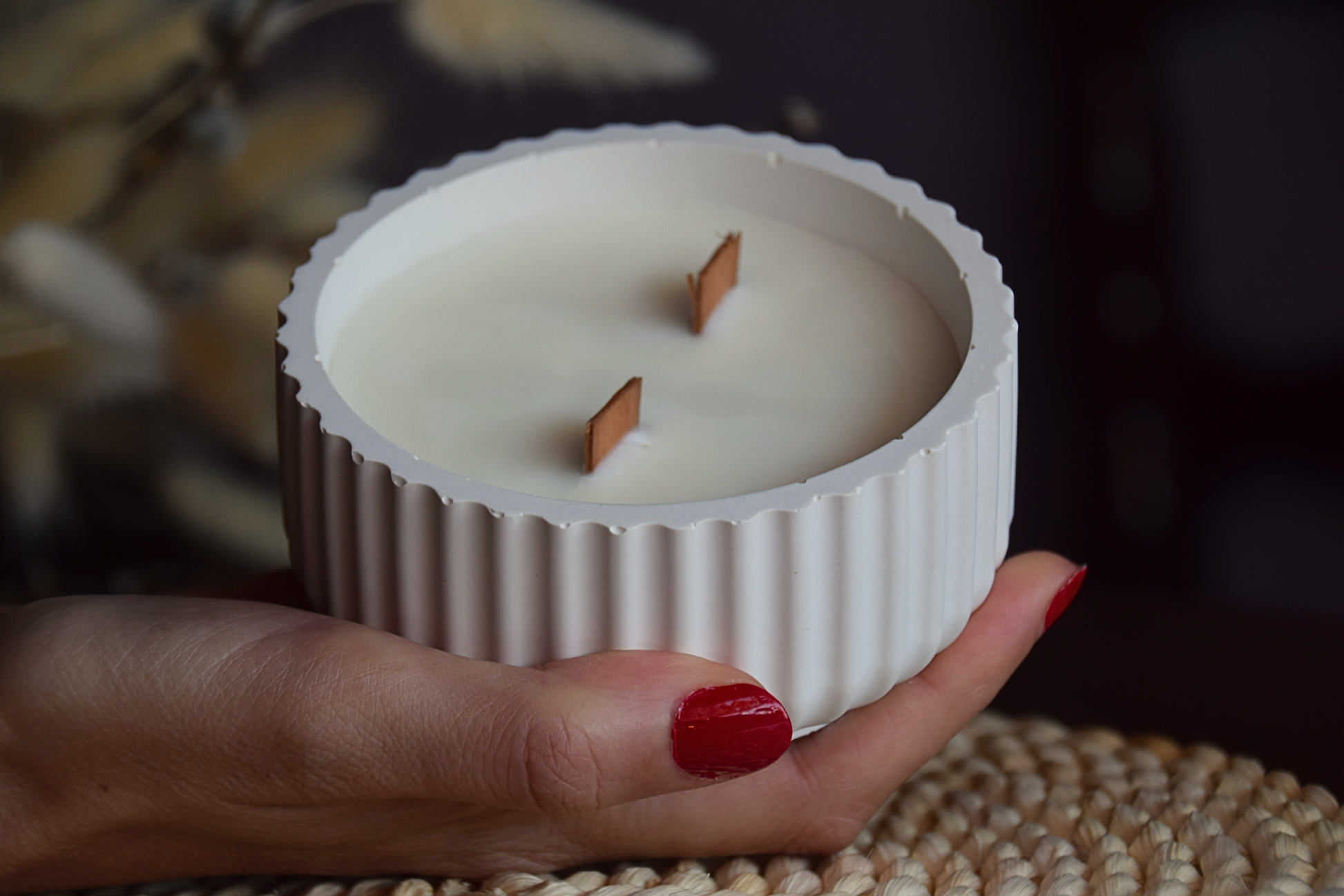 Vela decorativa en cuenco acanalado con mechas de madera sujetado por mano de modelo y fondo rustico.