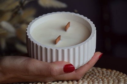 Vela decorativa en cuenco acanalado con mechas de madera sujetado por mano de modelo y fondo rustico.