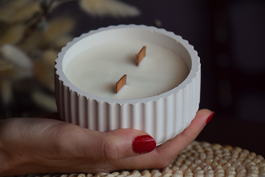 Vela decorativa en cuenco acanalado con mechas de madera sujetado por mano de modelo y fondo rustico.