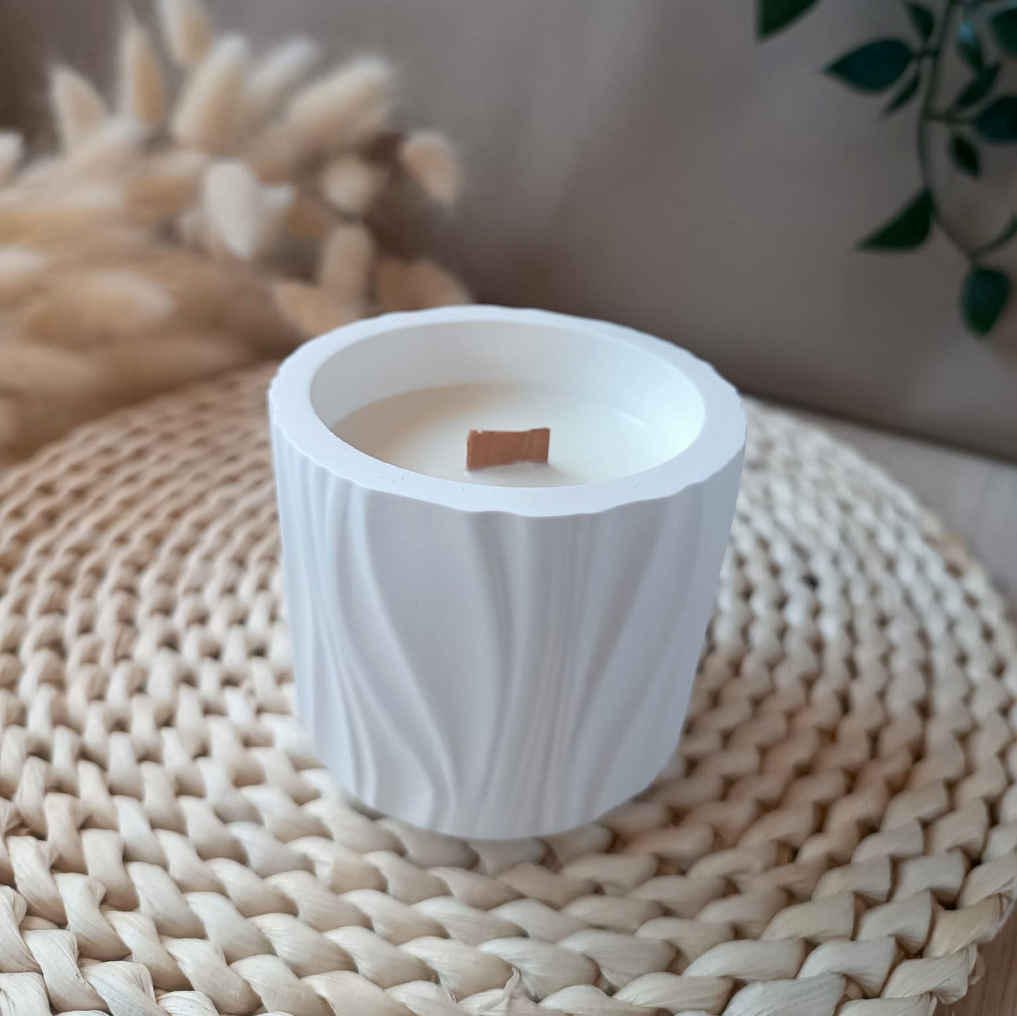 Vela decorativa de soja en recipiente de resina mineral blanco con textura de líneas suaves y mecha de madera en base de fibras naturales con fondo neutro