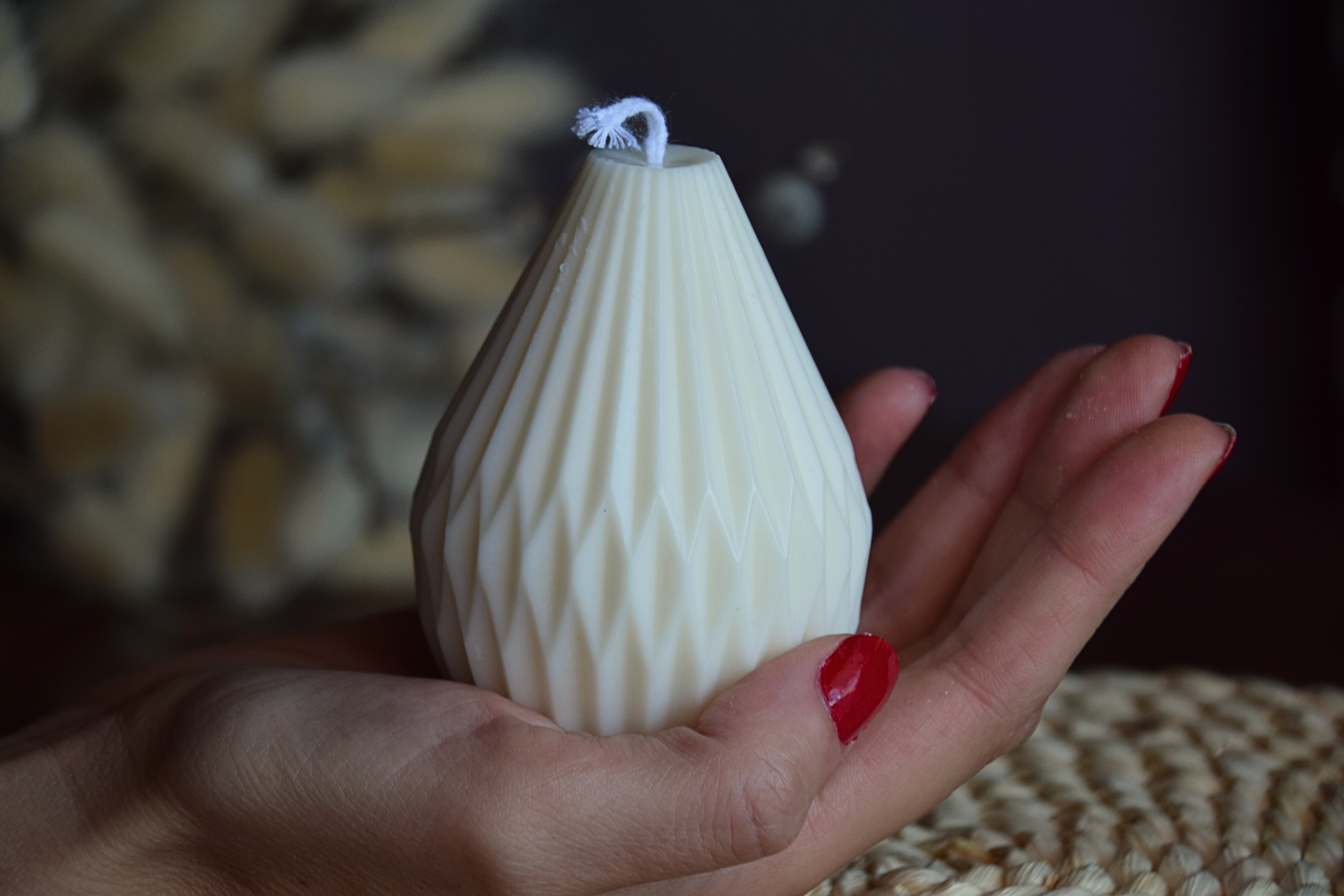 Vela decorativa de soja con formas geometricas y pabilo de algodon, sujeta por mano de modelo en fondo rustico.