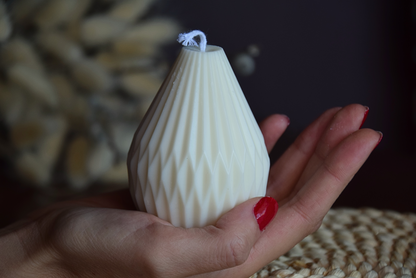 Vela decorativa de soja con formas geometricas y pabilo de algodon, sujeta por mano de modelo en fondo rustico.