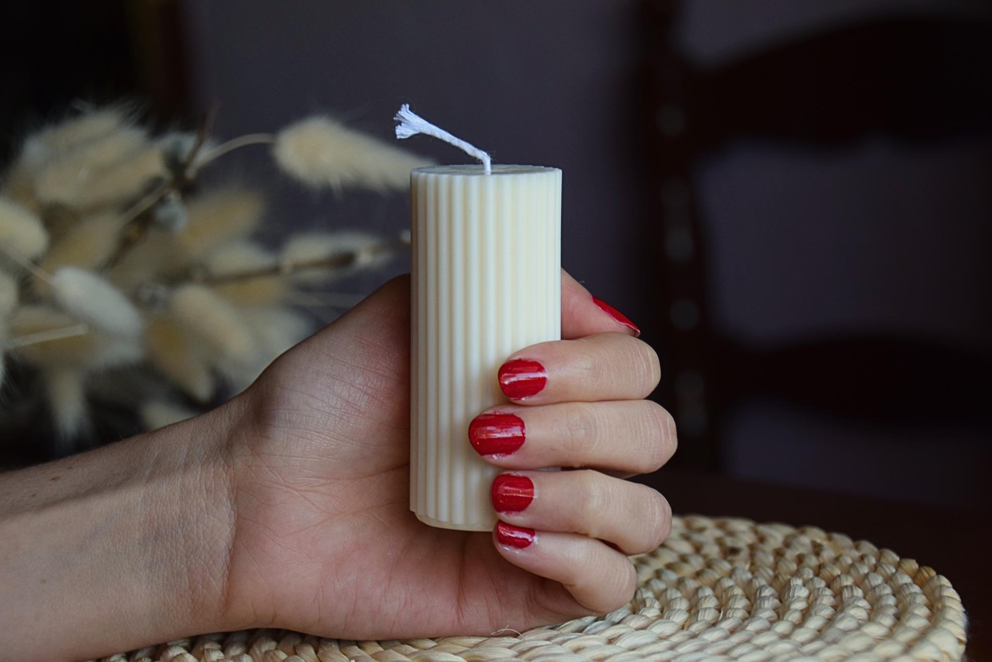 Vela decorativa pilar acanalado pequeño con pabilo de algodon sujeto por mano de modelo en fondo rustico.