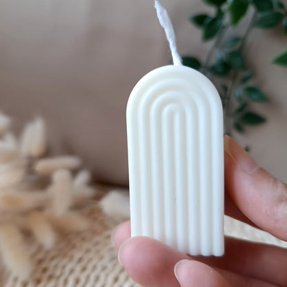 Vela artesanal de soja en forma de arco mini con diseño acanalado sostenida en la mano y fondo neutro