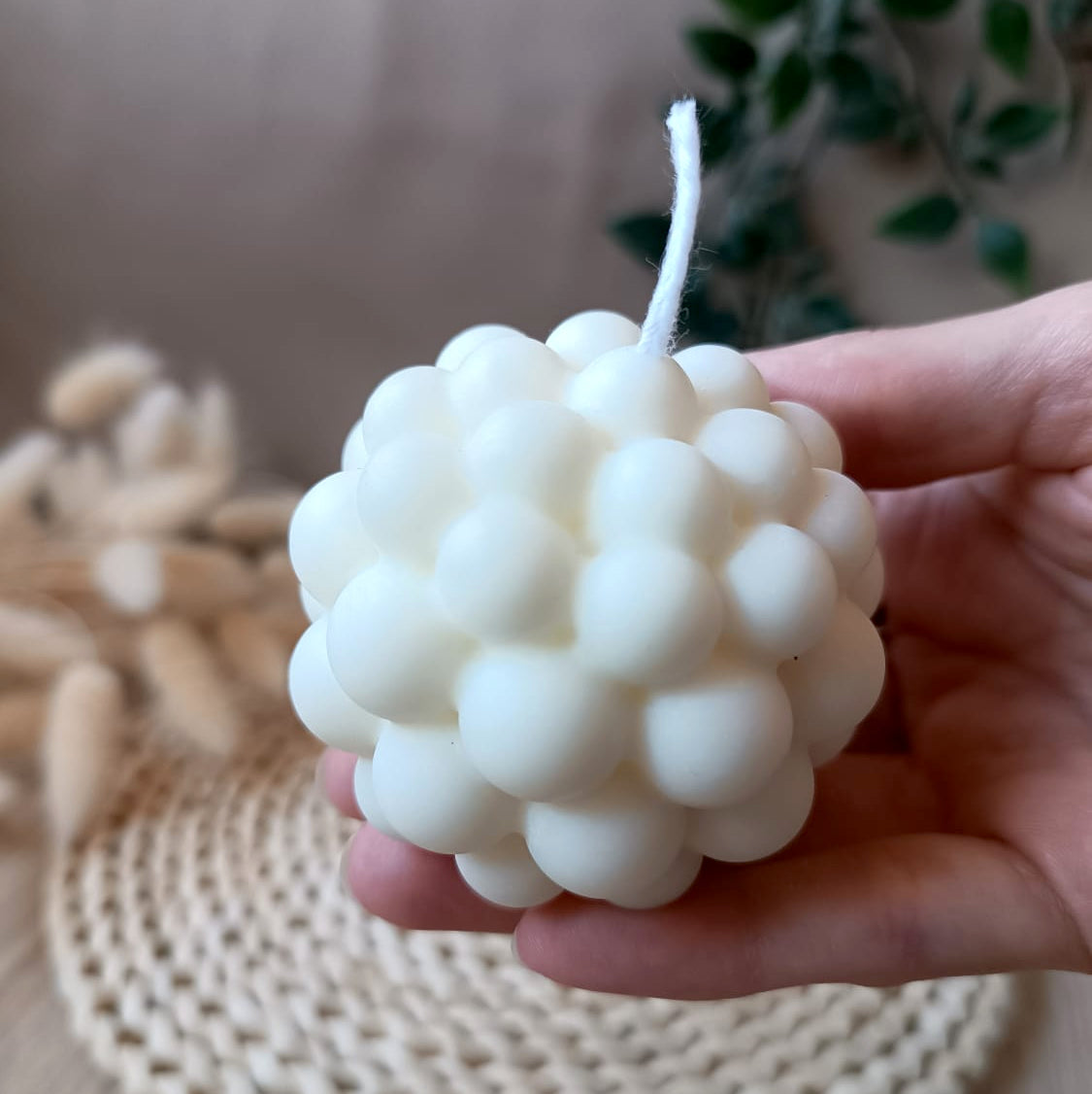 Vela artesanal de soja en forma de esfera con relieve de burbujas sostenida en la mano y fondo neutro