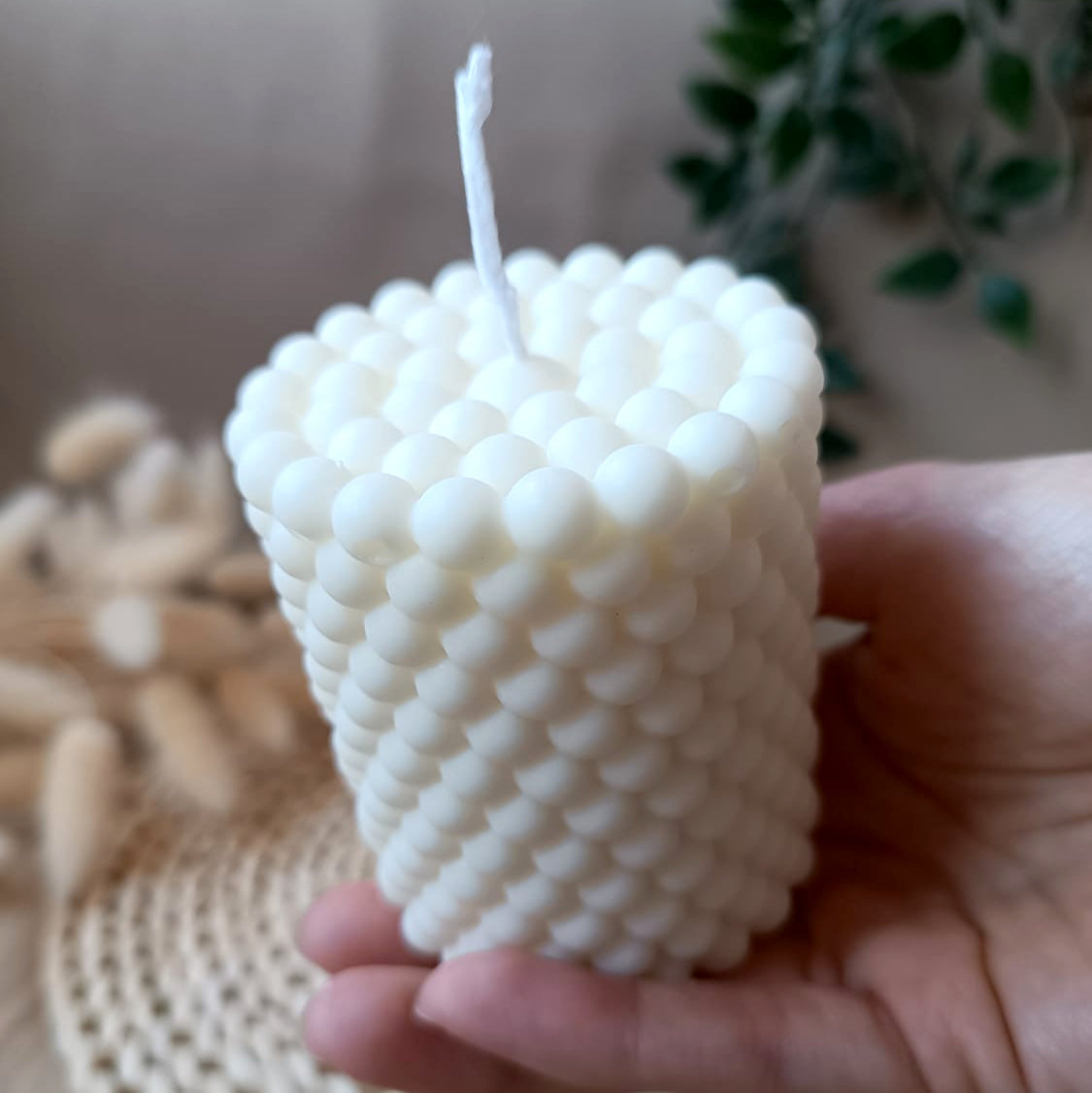 Vela artesanal de soja en forma de cono con relieve de burbujas sostenida en la mano y fondo neutro
