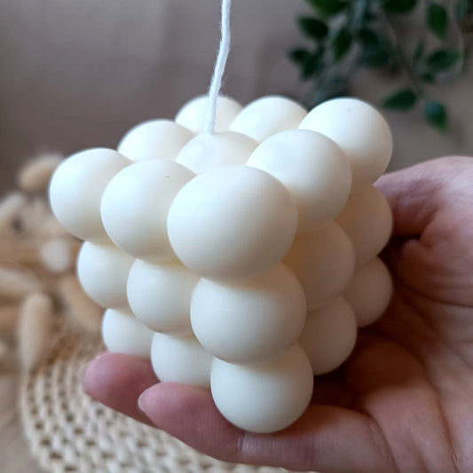 Vela artesanal de soja en forma de cubo con diseño de burbujas sostenida en la mano y fondo neutro