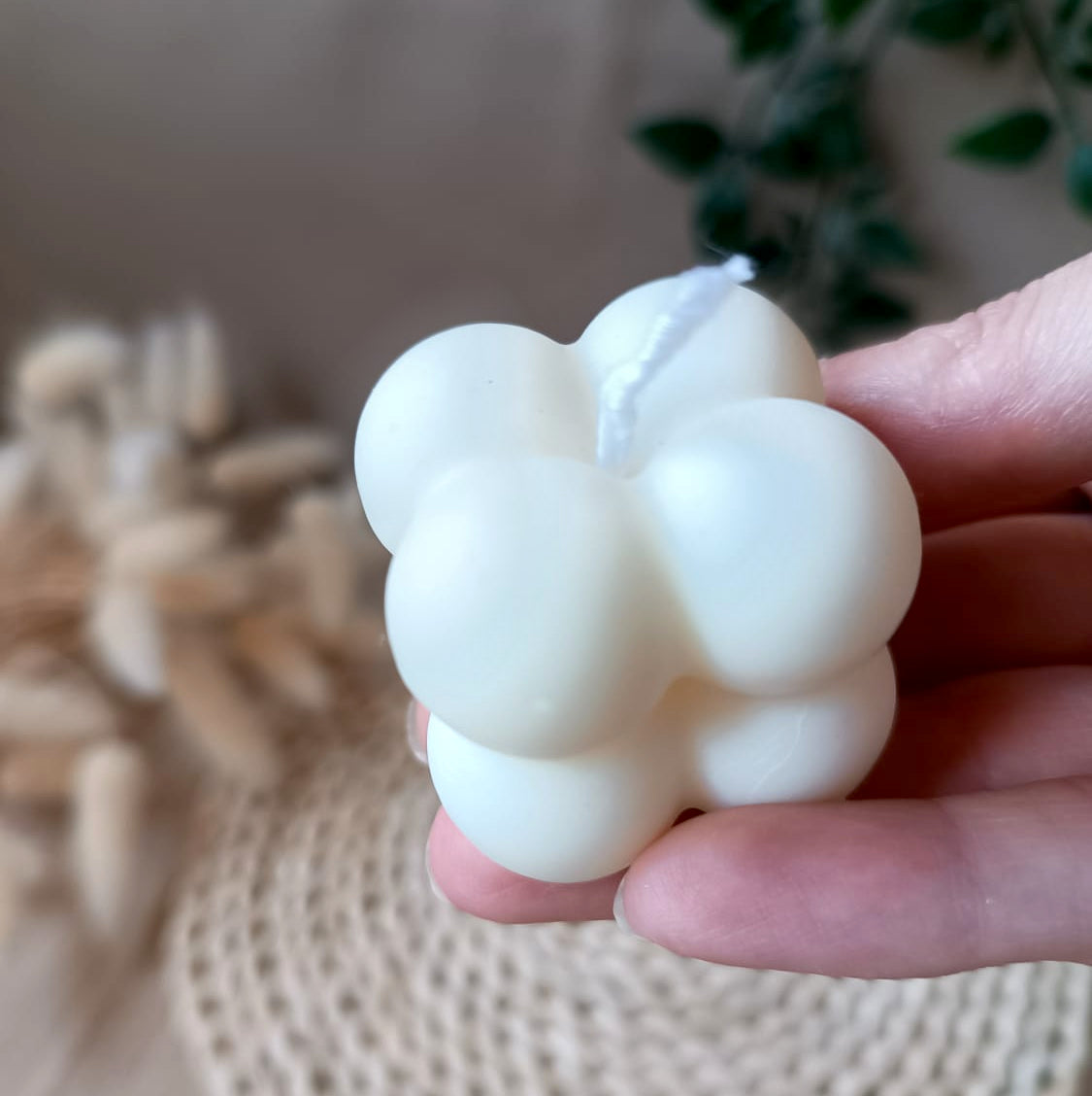 Vela de soja en forma de cubo con diseño de burbujas sostenida en la mano y fondo neutro