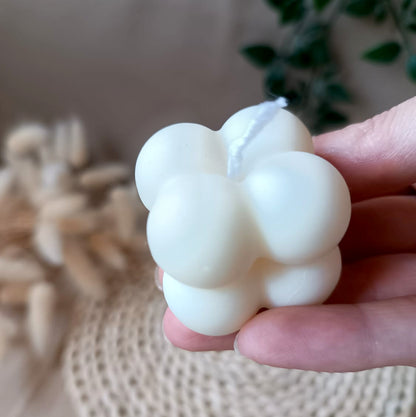 Vela de soja en forma de cubo con diseño de burbujas sostenida en la mano y fondo neutro
