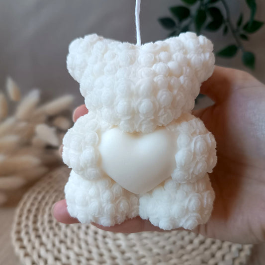 Vela natural de soja osito con corazón sostenida en la mano con fondo neutro