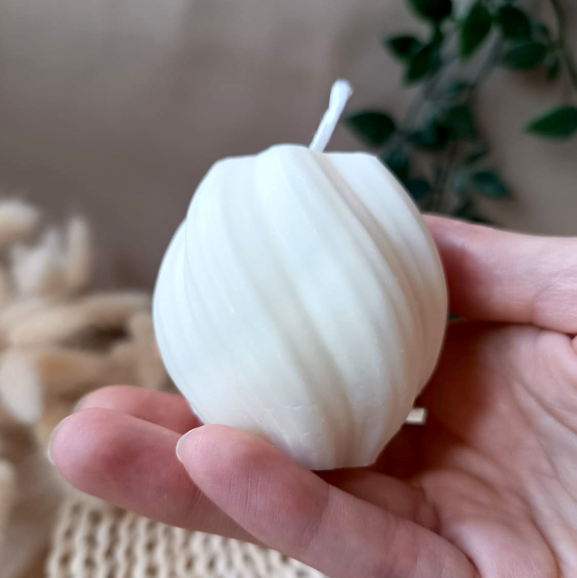 Vela natural de soja redonda con diseño espiral sostenida en la mano y fondo neutro
