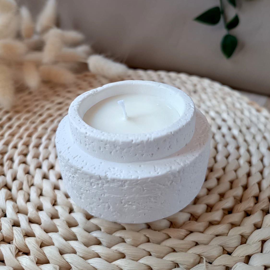 Vela de soja en recipiente blanco de resina mineral con textura efecto lava y mecha de algodón sobre base de fibras naturales y fondo neutro