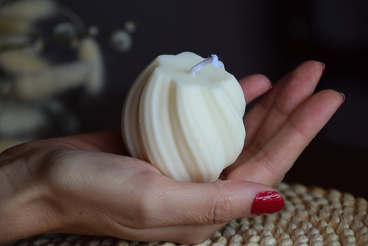 Vela decorativa pequeña en forma de tirabuzon con pabilo de algodon, sujetada por mano de modelo y presentada en fondo rustico. 