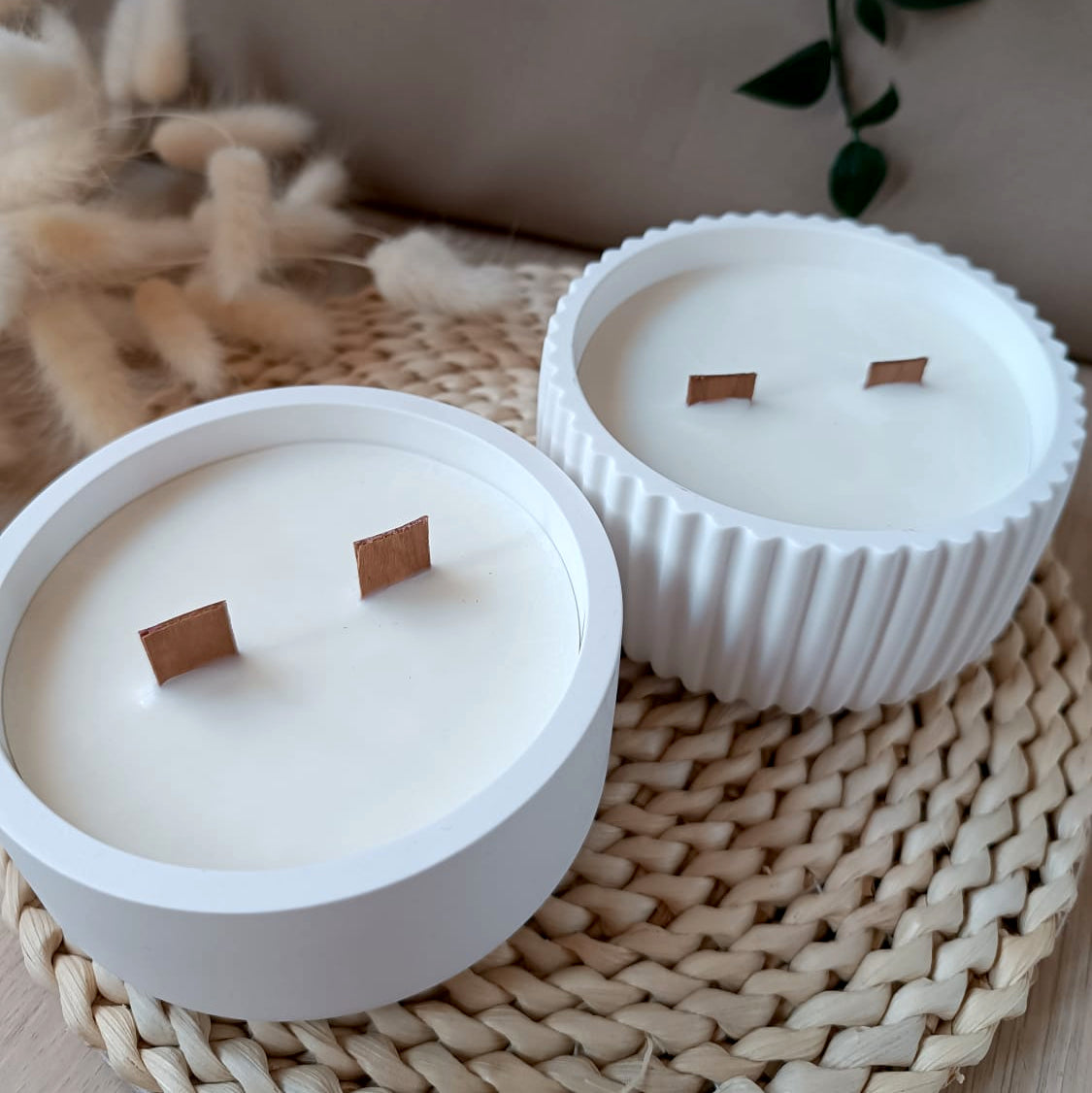 Vista superior de conjunto de velas decorativas de soja en recipiente de resina mineral liso y acanalado con doble mecha de madera sobre base de fibras naturales y fondo neutro