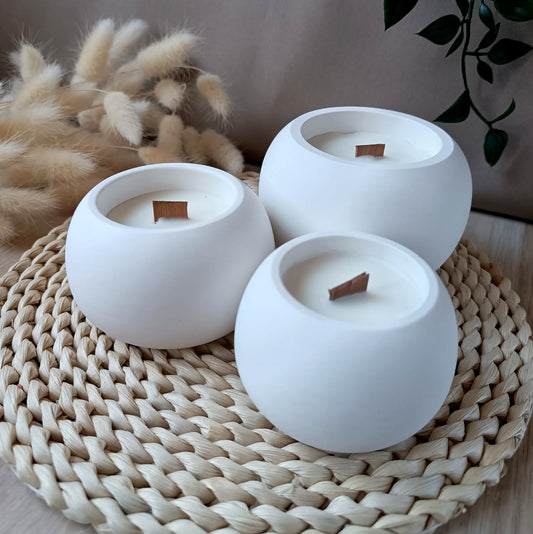 Conjunto de tres velas decorativas de soja en recipientes de distintas medidas de resina mineral con mecha de madera sobre base de fibras naturales y fondo neutro