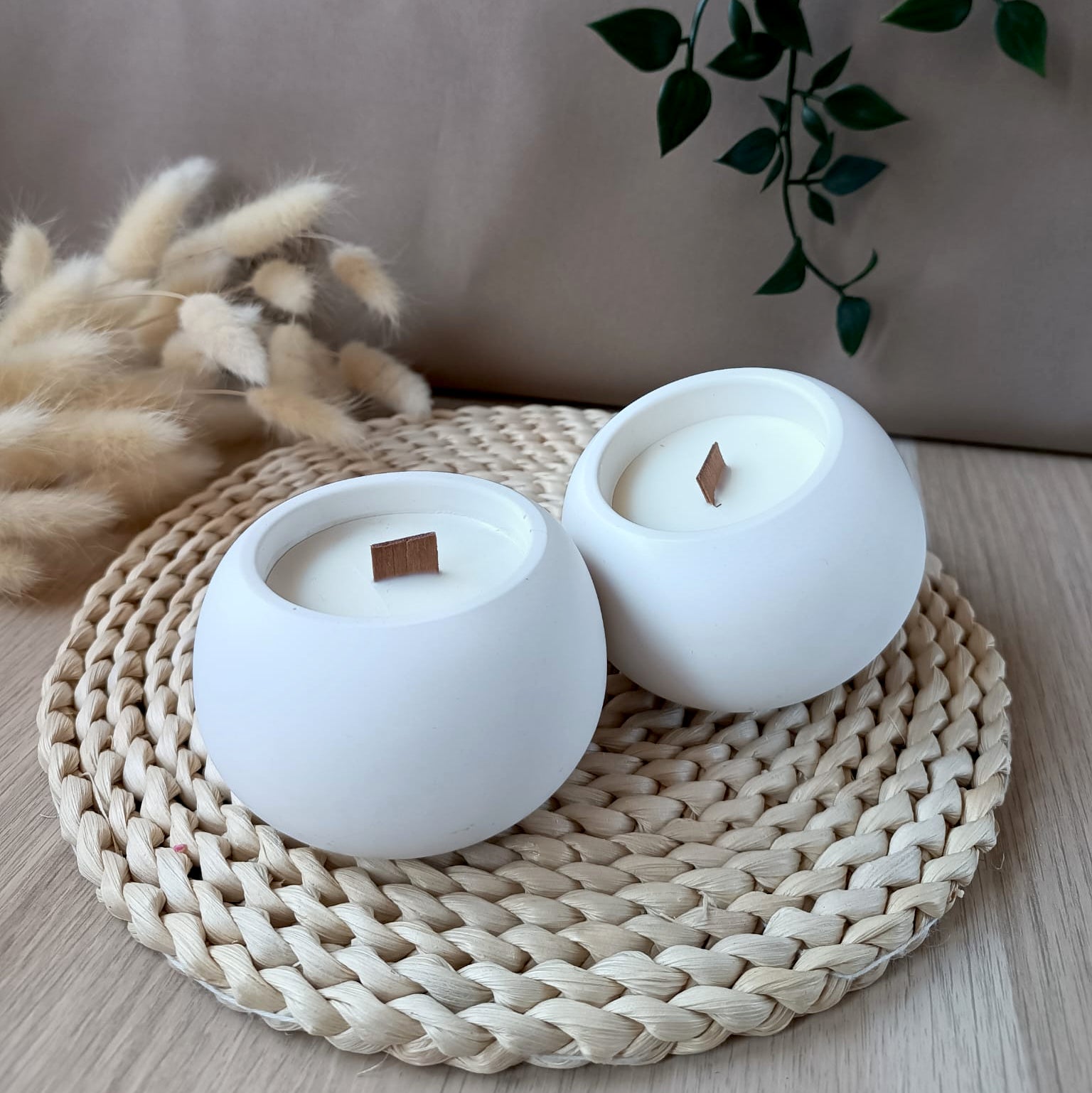 Conjunto de velas medianas redondas de soja en recipiente blanco liso de resina mineral con mecha de madera sobre base de fibras naturales y fondo neutro