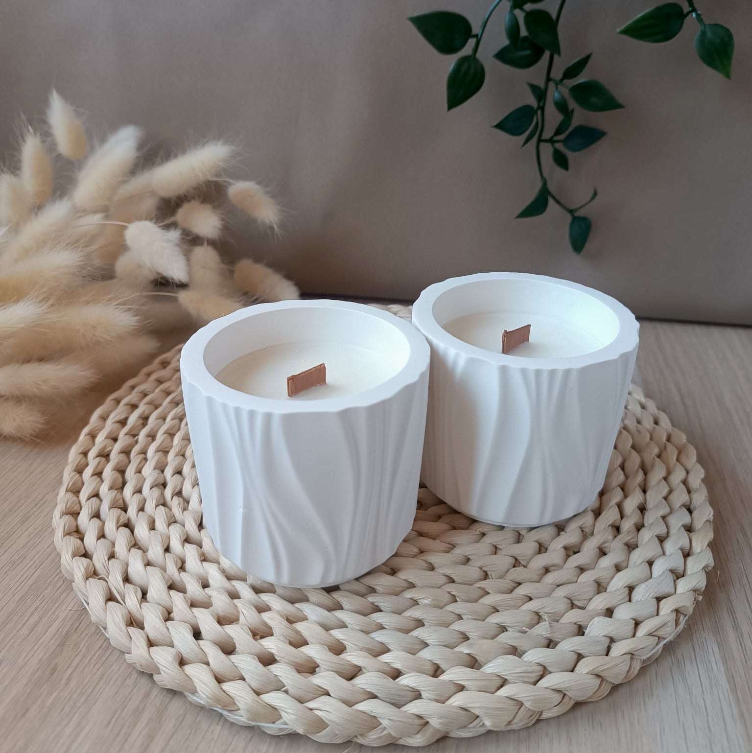Dos velas de soja en recipiente blanco de resina mineral con formas orgánicas y mecha de madera en base de fibras naturales y fondo neutro