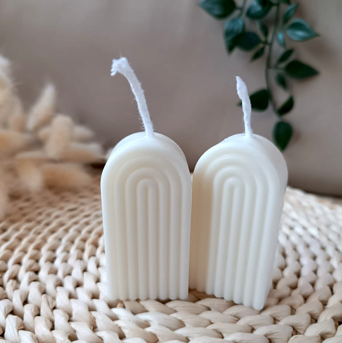 Dos velas decorativas de soja en forma de arco con relieve lineal sobre base de fibras naturales y fondo neutro
