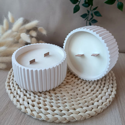 Dos velas grandes de soja en bol blanco de resina mineral con relieve de rayas y doble mecha de madera sobre base de fibras naturales y fondo neutro