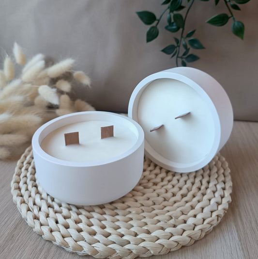 Dos velas grandes de soja en bol blanco liso de resina mineral con doble mecha de madera sobre base de fibras naturales y fondo neutro