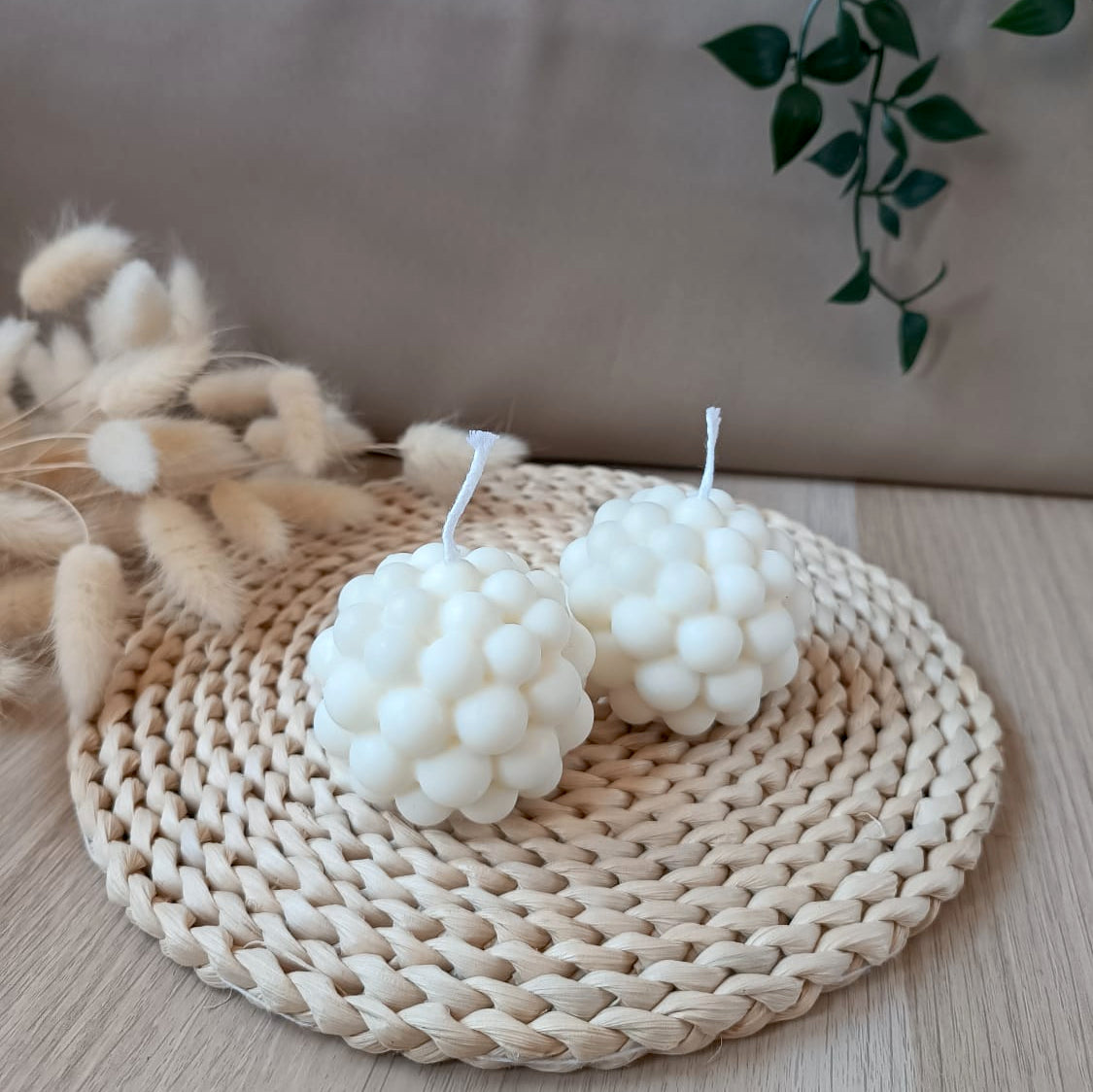 Dos velas decorativas de soja en forma de esfera con diseño de burbujas sobre base de fibras naturales y fondo neutro