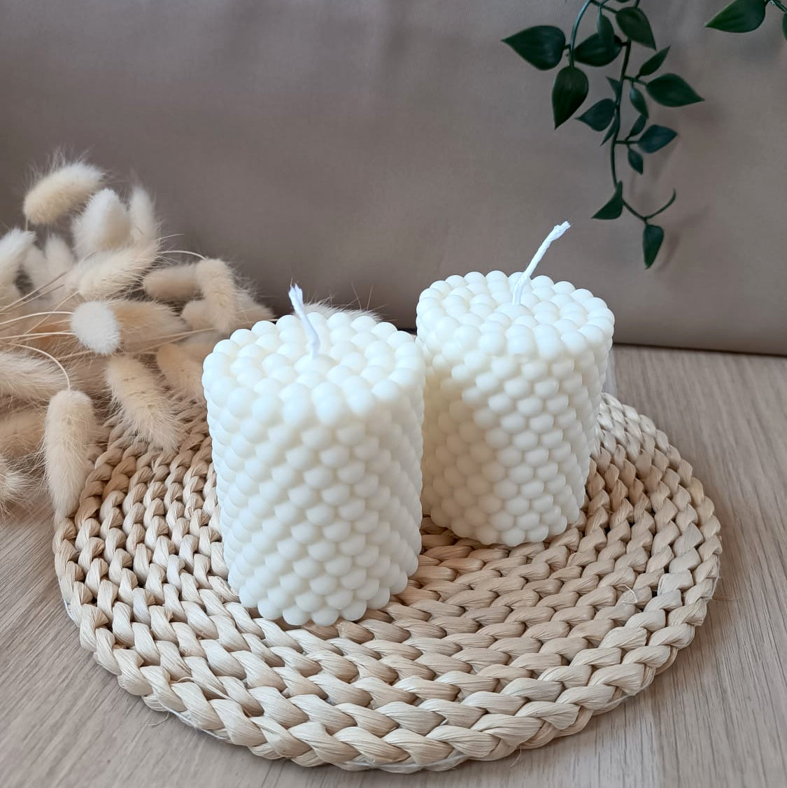 Dos velas decorativas de soja en forma de cono con diseño de burbujas sobre base de fibras naturales y fondo neutro