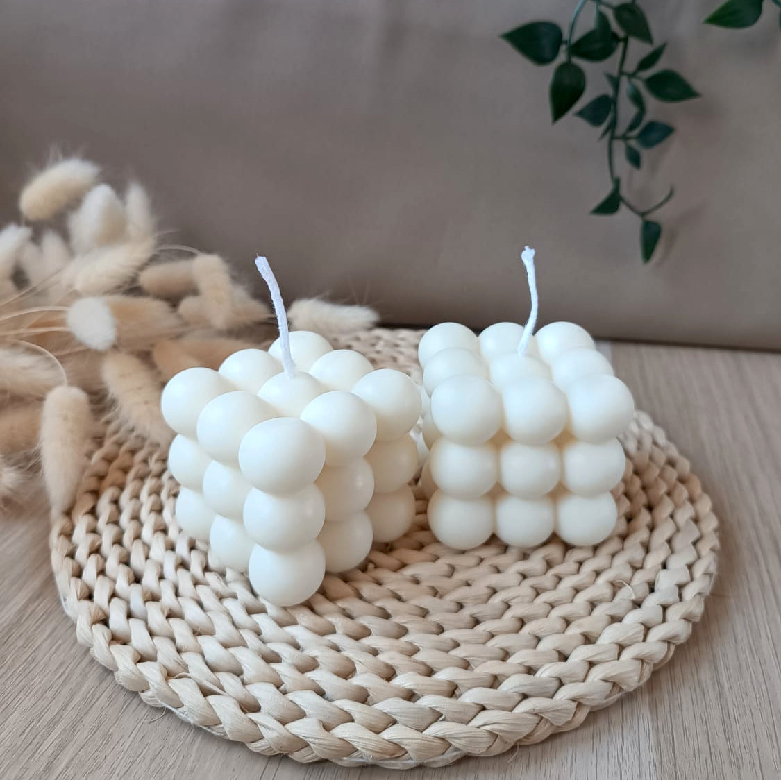 Dos velas decorativas de soja en forma de cubo con diseño de burbujas sobre base de fibras naturales y fondo neutro