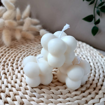 Tres velas decorativas de soja en forma de cubo con diseño de burbujas sobre base de fibras naturales y fondo neutro