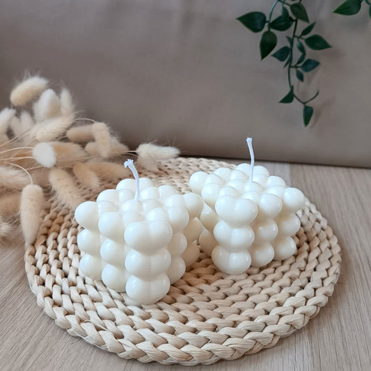 Dos velas decorativas de soja en forma de cubo con relieve de corazones sobre base de fibras naturales y fondo neutro