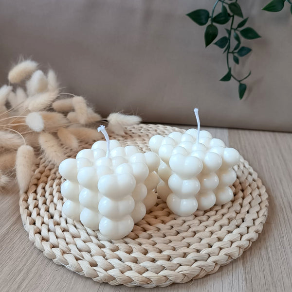 Dos velas decorativas de soja en forma de cubo con relieve de corazones sobre base de fibras naturales y fondo neutro