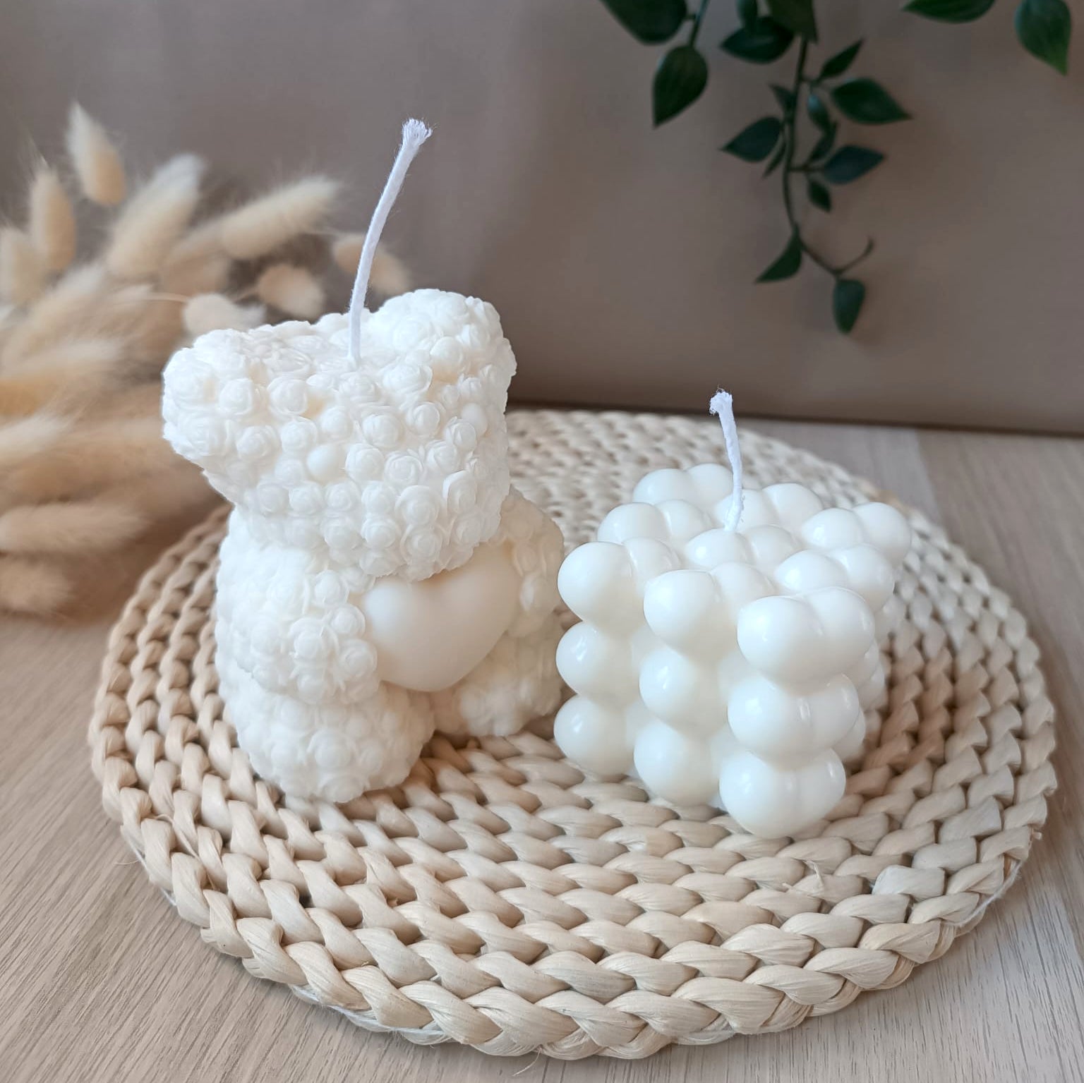 Conjunto de velas decorativas de soja compuesto por vela en forma de oso con textura de flores con corazon y vela en forma de cubo con corazones sobre base de fibras naturales y fondo neutro