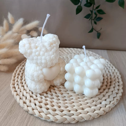 Conjunto de velas decorativas de soja compuesto por vela en forma de oso con textura de flores con corazon y vela en forma de cubo con corazones sobre base de fibras naturales y fondo neutro