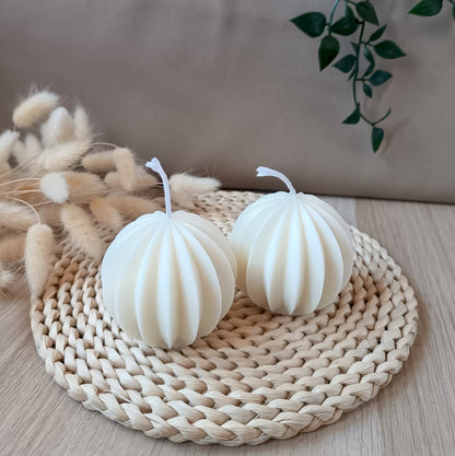 Dos velas decorativas de soja en forma de esfera geométrica sobre base de fibras naturales y fondo neutro
