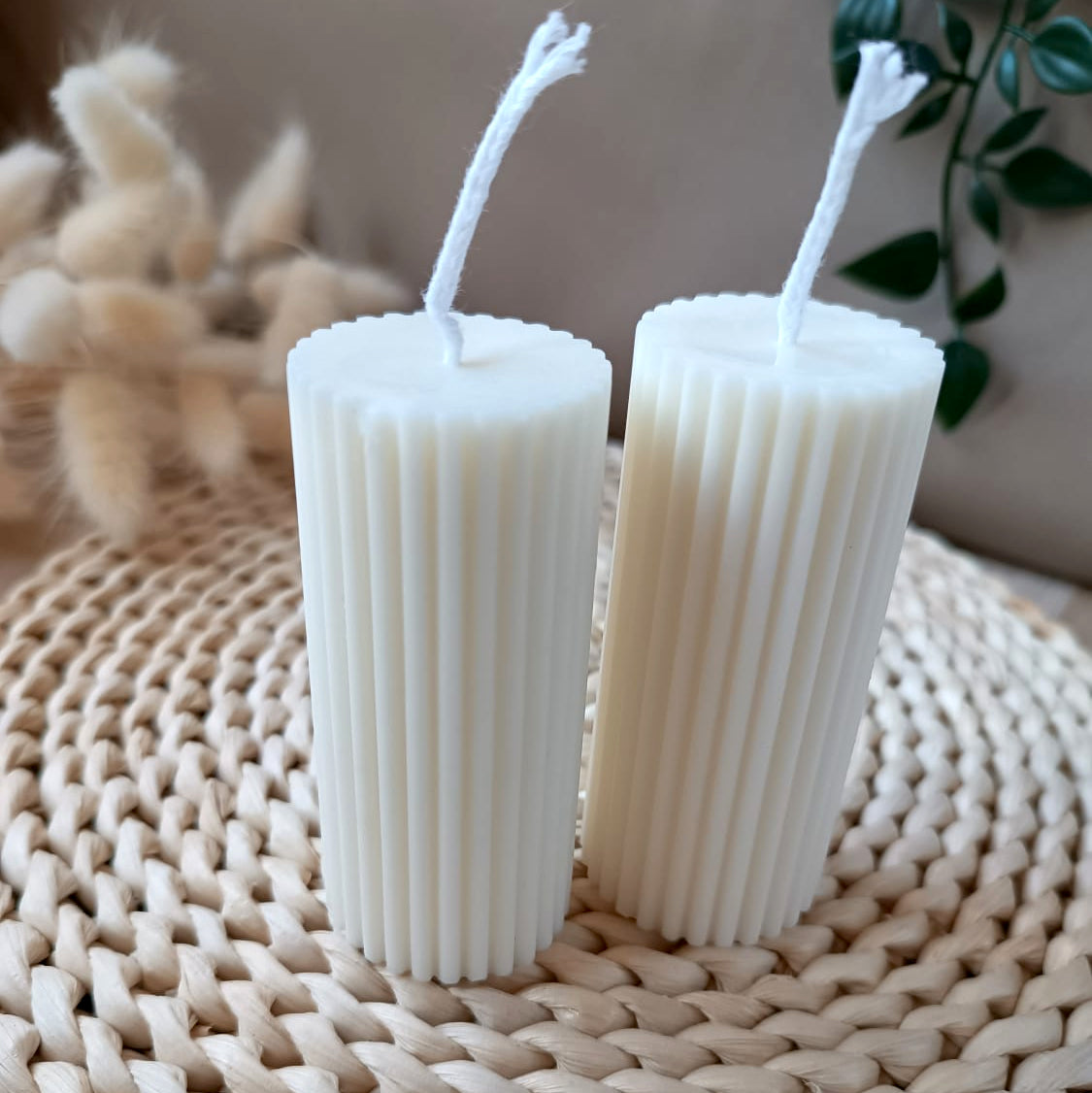 Dos velas decorativas de soja tipo pilar con relieve vertical sobre base de fibras naturales y fondo neutro